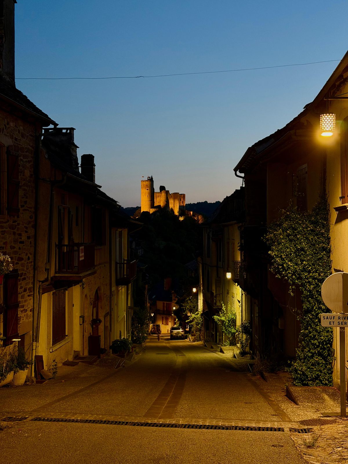 Une rue de Najac au crépuscule, avec la forteresse illuminée au bout de la rue